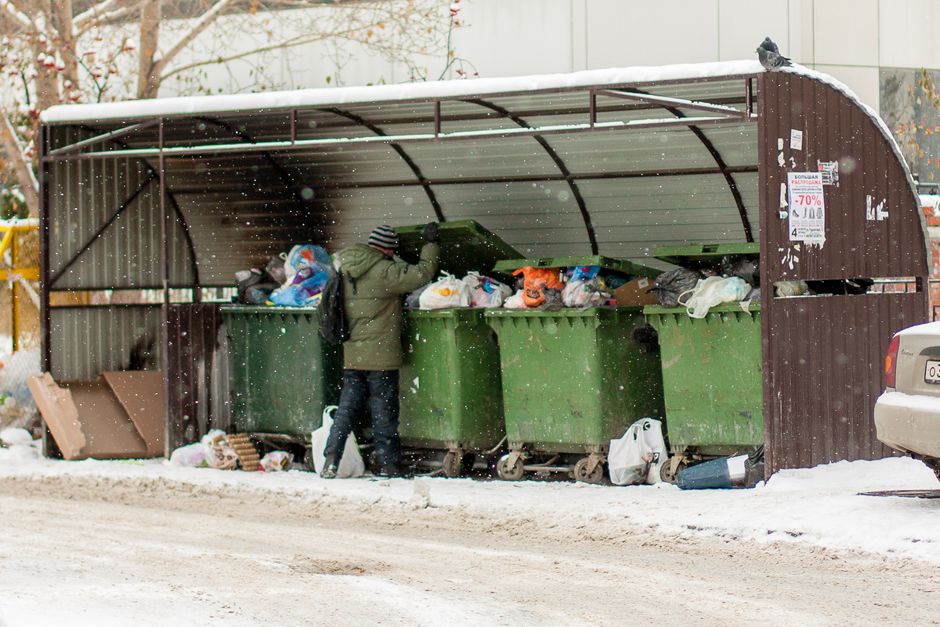 Three large outdoor waste containers situated on a pavement in front of a residential building, with two yellow bins on the left and a green bin on the right. The yellow containers are made of durable